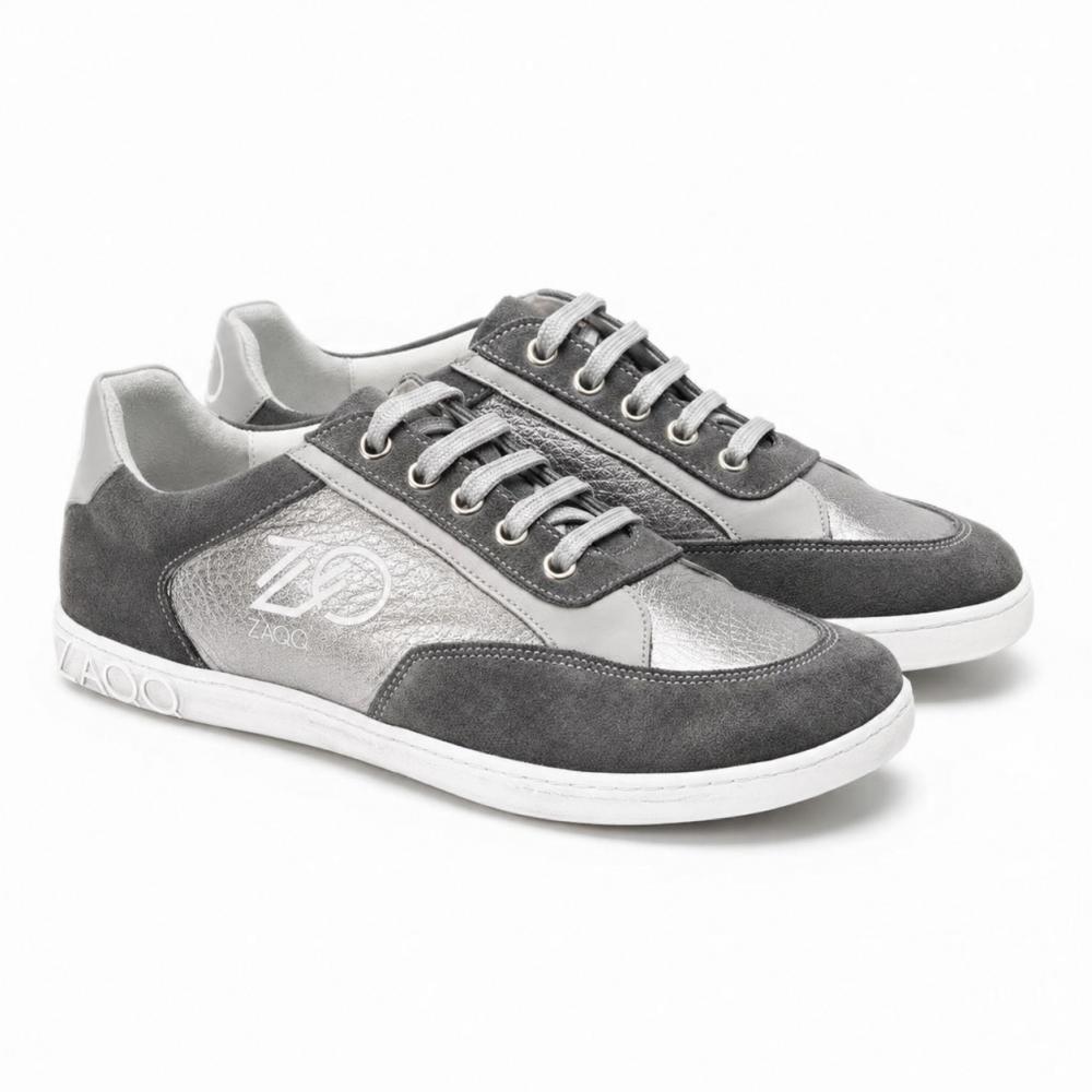 Ein Paar OQTAV Grey-Sneaker von ZAQQ, gefertigt aus samtigem Wildleder und strukturierten Einsätzen. Mit silbernen Schnürsenkeln und dem unverwechselbaren Zagoo-Logo an der Seite und der Ferse werden diese stilvollen Schuhe nebeneinander auf einem weißen Hintergrund präsentiert.