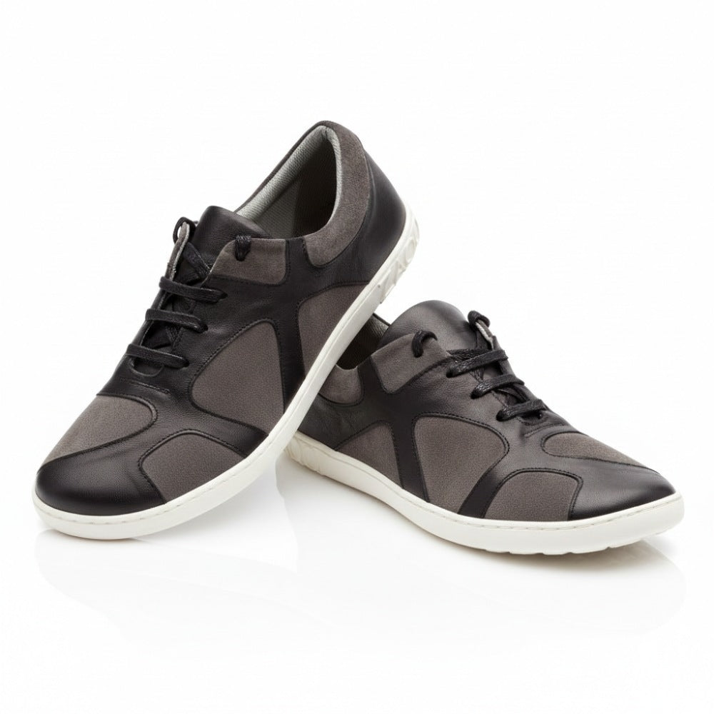 Wir präsentieren den QAANAAQ Black von ZAQQ, ein Paar stylische Sneaker aus luxuriösem Veloursleder in Grau und Schwarz, ergänzt durch weiße Sohlen. Die Schuhe werden so präsentiert, dass einer hoch steht, während der andere dagegen lehnt, was ein modernes und elegantes Design mit schwarzen Schnürsenkeln und einem strukturierten Muster hervorhebt. Diese leichten Sneaker verbinden nahtlos Eleganz mit Komfort.