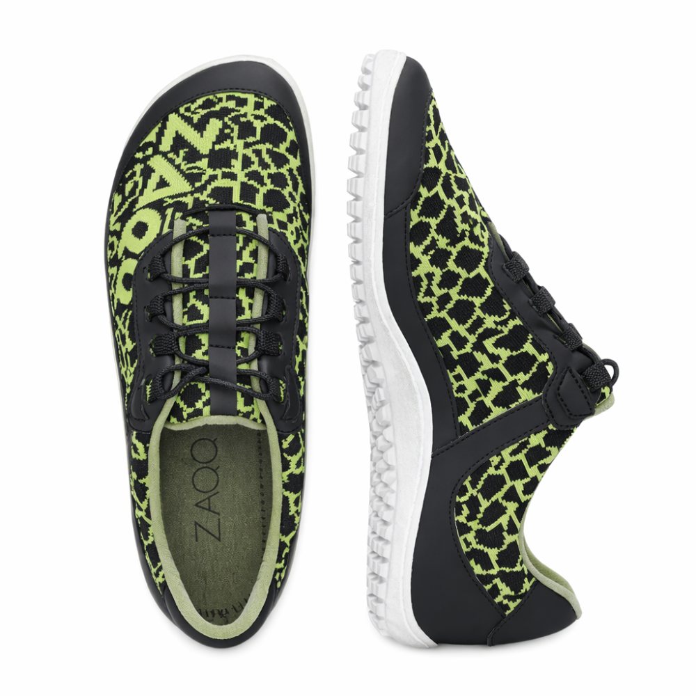 Die QASEY Green von ZAQQ sind ein Paar Schuhe mit einem schwarz-grünen Pixelmuster aus veganen Materialien. Sie haben schwarze Schnürsenkel, eine schwarze Sohle mit weißen Akzenten und das Wort ZAO ist auf der Innenseite sichtbar. Ein Schuh ist von oben zu sehen, während der andere sein Seitenprofil zeigt.