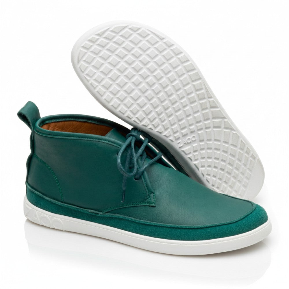 Ein Paar stylische knöchelhohe QUITMAN Green-Sneakers aus Velours- und Glattleder von ZAQQ mit grauer Sohle. Ein Schuh steht aufrecht und zeigt seine Schnürsenkel, während der andere geneigt ist und die Sohle mit Waffelmuster und dem Markennamen ZAQQ zeigt.
