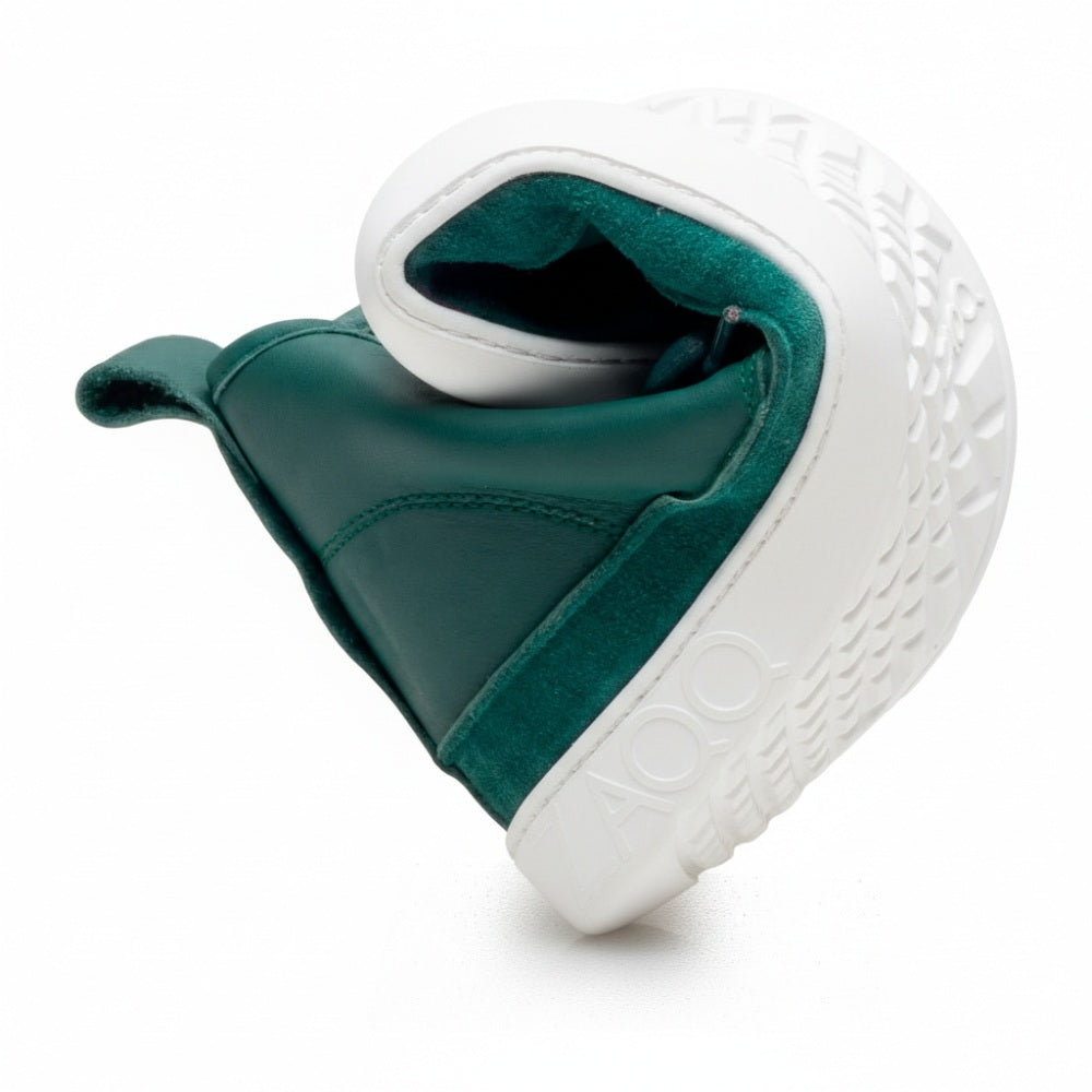 Wir präsentieren die QUITMAN Green Stiefeletten von ZAQQ, gefertigt aus einer Kombination aus Velours und Glattleder. Diese stylischen Schuhe haben graue Schnürsenkel und eine leicht abgenutzte weiße Gummisohle und verbinden das elegante Design von Sneakers mit einer bequemen Passform, wunderschön präsentiert auf einem weißen Hintergrund.