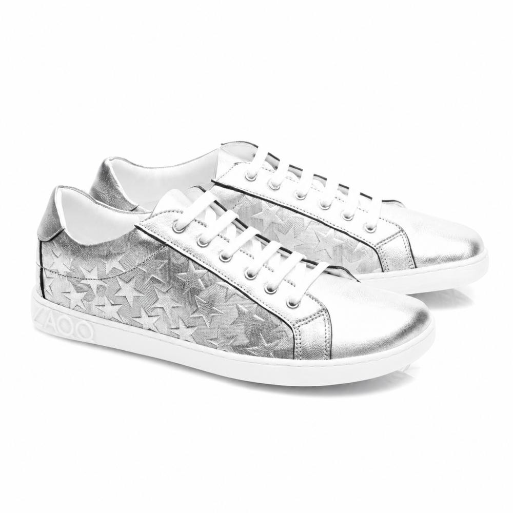 Die SLOQ Stars Silver-Sneaker von ZAQQ haben weiße Schnürsenkel und Sternmuster an den Seiten, ergänzt durch eine weiße Sohle mit VAOO-Prägung an der Ferse. Diese Schuhe zeichnen sich durch ein schlankes und modernes Design mit einem glänzenden Metallic-Finish aus.