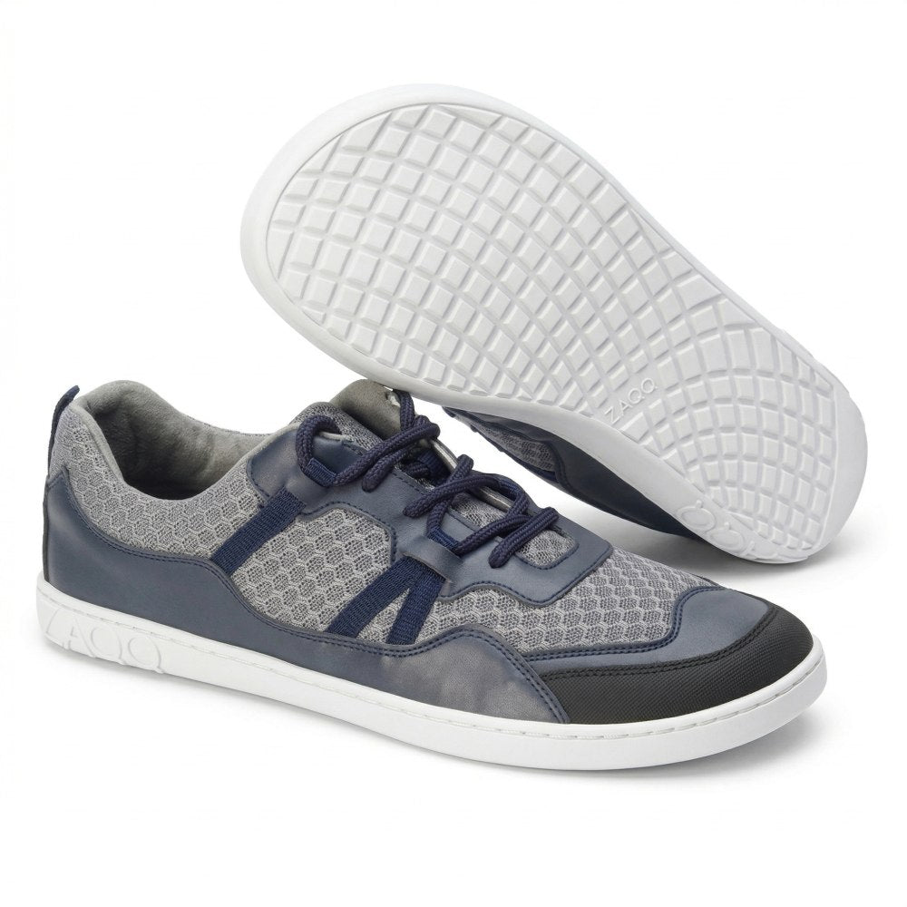 Ein Paar SQATE Grey-Sneaker von ZAQQ mit schicken grauen und blauen Mesh-Akzenten und weißen Sohlen. Ein Schuh ist seitlich positioniert, um das Gittermuster auf der Sohle zu zeigen, während der andere aufrecht steht, um die Schnürsenkel und das Obermaterialdesign hervorzuheben.