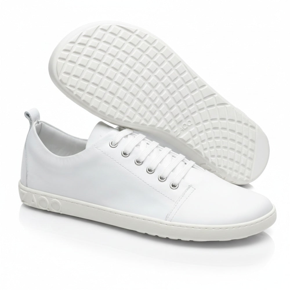 Ein Paar TAQQ Nappa White Sneaker von ZAQQ aus hochwertigem Nappaleder mit strukturiertem Muster und grauen Sohlen. Der linke Barfußschuh steht aufrecht und zeigt die Seitenansicht mit dem ZAQQ-Label auf der flexiblen Kautschuksohle, während der rechte Schuh geneigt ist, um das Design der unteren Sohle zu zeigen.